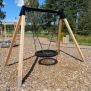 Single Swing (BNS 90cm) schommel met houten frame en zwart zitvlak op een speelplaats.