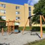 Single Swing (BNS 90cm) schommel met houten frame en zwart zitvlak op een speelplaats.